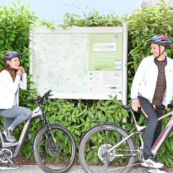 Zwei Radfahrer vor einem Informationstafel in Stegersbach, bereit für eine Radtour.