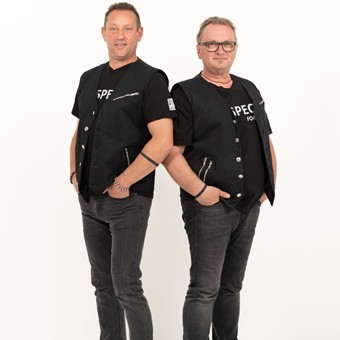 Zwei schwarz gekleidete Männer stehen nebeneinander und lächeln.