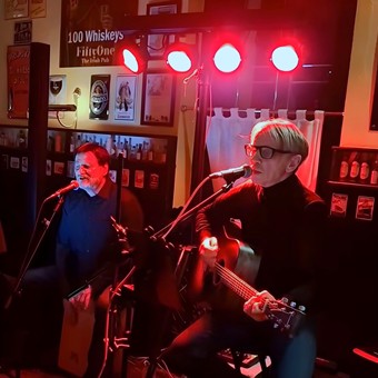 Zwei Musiker auf der Bühne, einer mit Gitarre und der andere mit Cajón.