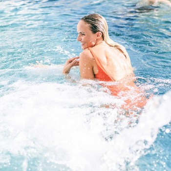 Dive in and let go Smiling woman in an orange swimsuit relaxing in the bubbling thermal water of the outdoor pool.