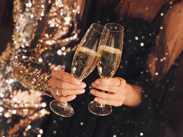 Zwei Frauen in festlichen Paillettenkleidern stoßen mit zwei Gläsern prickelndem Sekt auf das neue Jahr an.