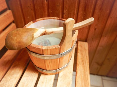 A wooden infusion bucket with a ladle sits ready for a soothing sauna session in a classically designed wooden sauna.