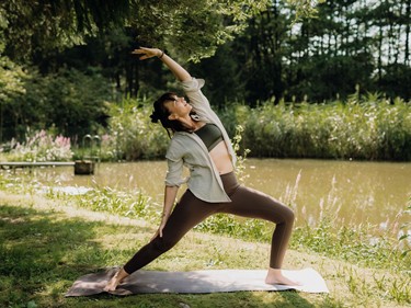Eine Frau macht Yoga auf einer Wiese unter einem Baum.
