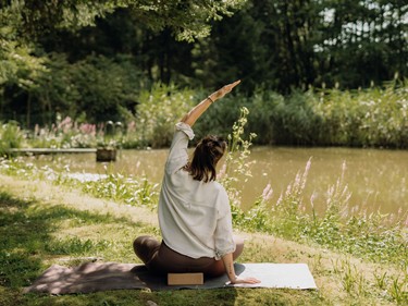 Eine Frau macht Yoga auf einer Wiese vor einem Teich.