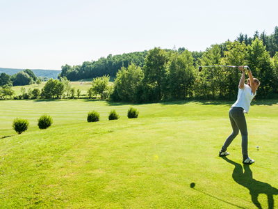 Eine Golfspielerin führt einen kraftvollen Abschlag auf dem weitläufigen, grünen Fairway der Golfschaukel Stegersbach aus.
